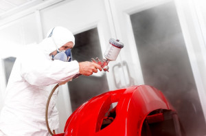 mechanic painting a red bumper of a car in workshop
